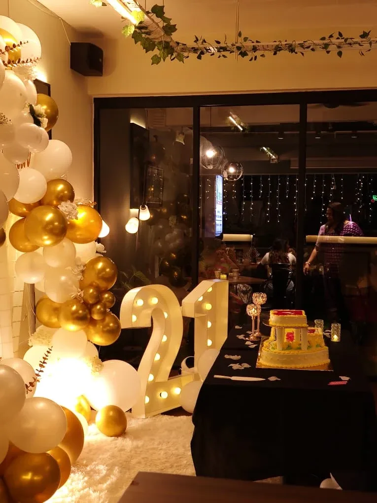 A birthday party set up at Kiya's TTDI, with gold and white balloons, a lit-up 21 and a tiered cake